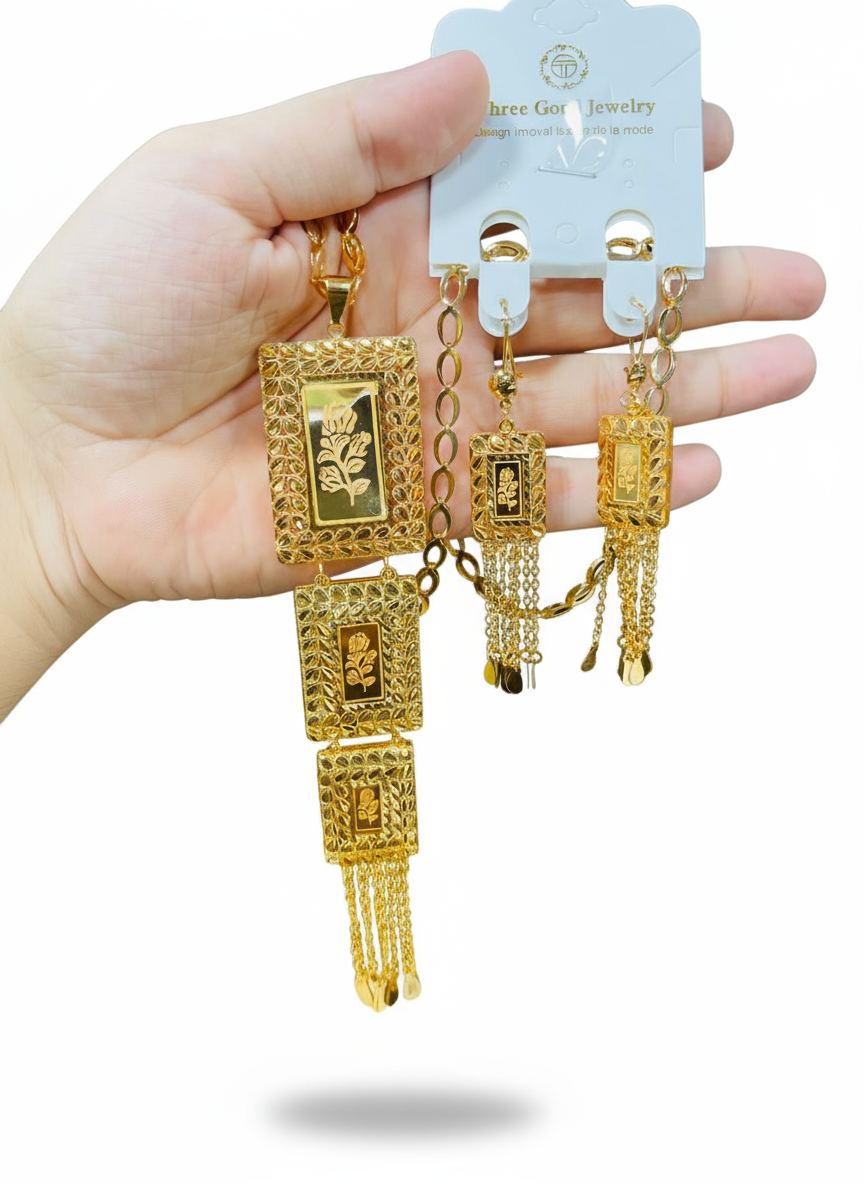 Gold earrings held by a hand with a visible brand label on a white background