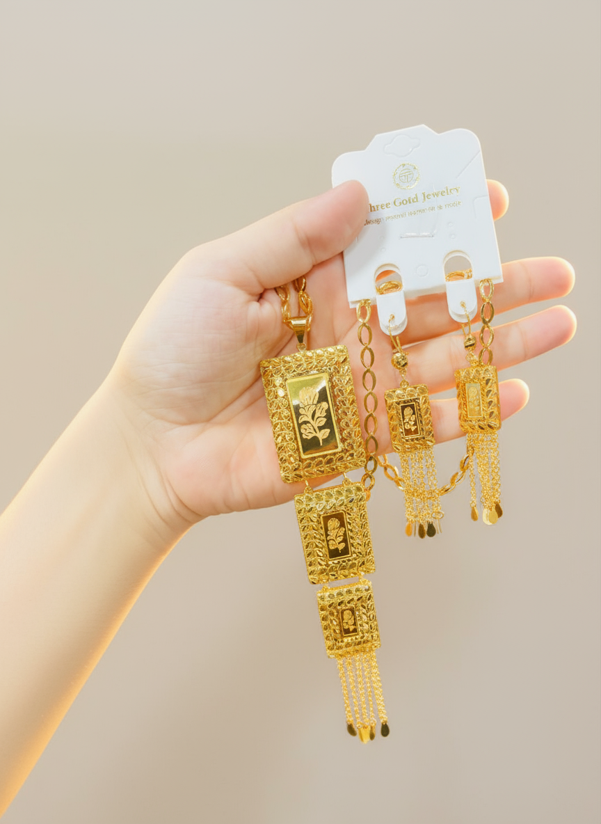 Gold bracelet and earrings held by a hand with a beige background