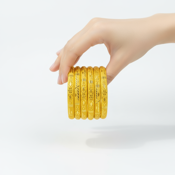 Hand holding five gold bangles against a white background