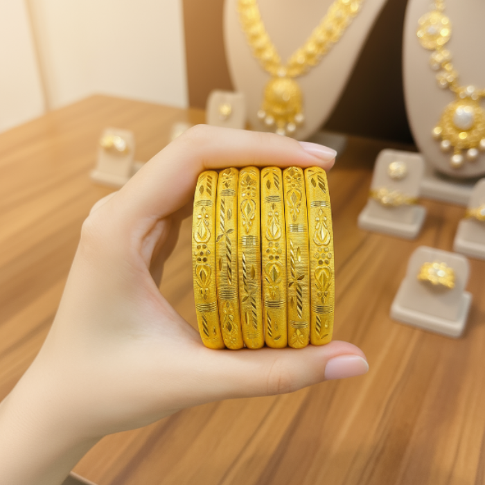 Hand holding four gold bangles with a jewelry display in the background